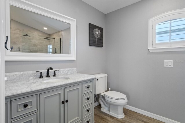 bathroom with tiled shower, wood-type flooring, vaulted ceiling, vanity, and toilet