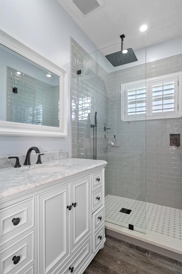 bathroom with tiled shower, hardwood / wood-style flooring, and vanity