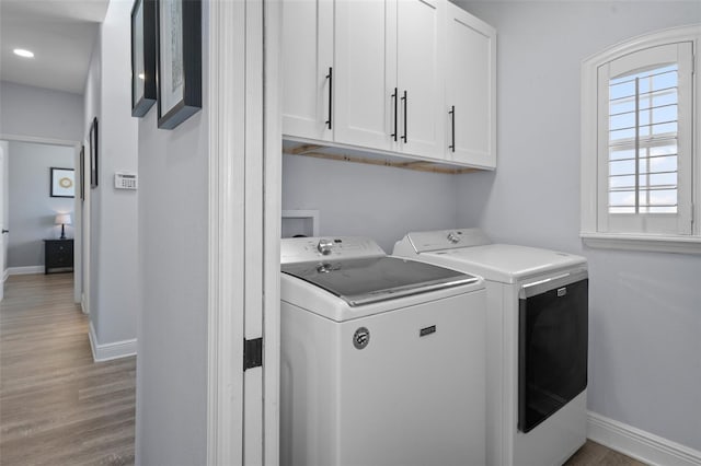 clothes washing area with cabinets, wood-type flooring, and washer and dryer