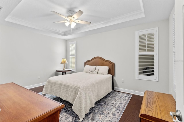 bedroom featuring dark hardwood / wood-style flooring, ceiling fan, crown molding, and a tray ceiling