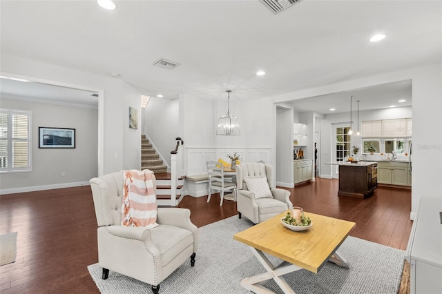 living room featuring dark hardwood / wood-style flooring, an inviting chandelier, a healthy amount of sunlight, and crown molding