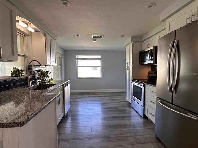 kitchen with dark stone countertops, white cabinetry, stainless steel appliances, sink, and dark wood-type flooring