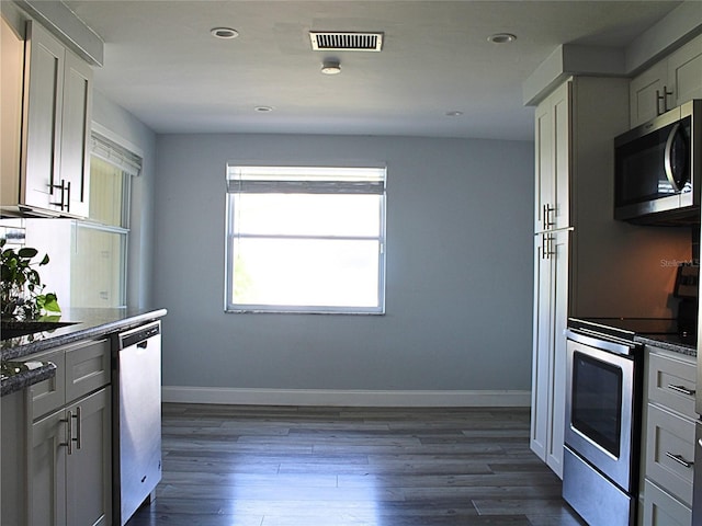 kitchen featuring dark wood-type flooring, stainless steel appliances, and dark stone counters