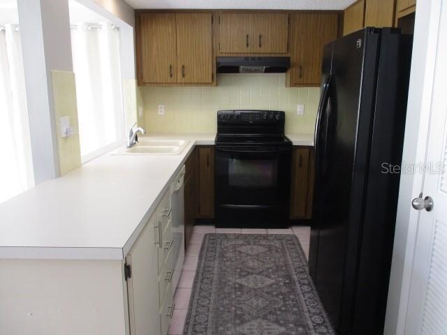 kitchen with light tile patterned floors, sink, black appliances, kitchen peninsula, and tasteful backsplash