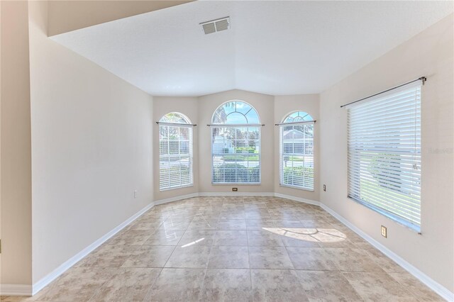 spare room featuring baseboards, visible vents, vaulted ceiling, and light tile patterned floors
