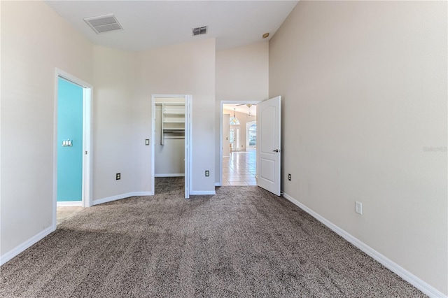 unfurnished bedroom featuring a walk in closet, carpet flooring, high vaulted ceiling, and a closet