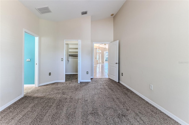 unfurnished bedroom featuring high vaulted ceiling, carpet floors, a walk in closet, baseboards, and visible vents