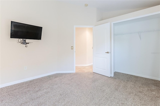 unfurnished bedroom with carpet flooring, a closet, baseboards, and lofted ceiling