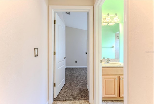 hallway featuring a sink, baseboards, light colored carpet, and visible vents