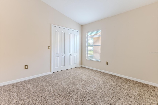 unfurnished bedroom with a closet, carpet, lofted ceiling, and baseboards