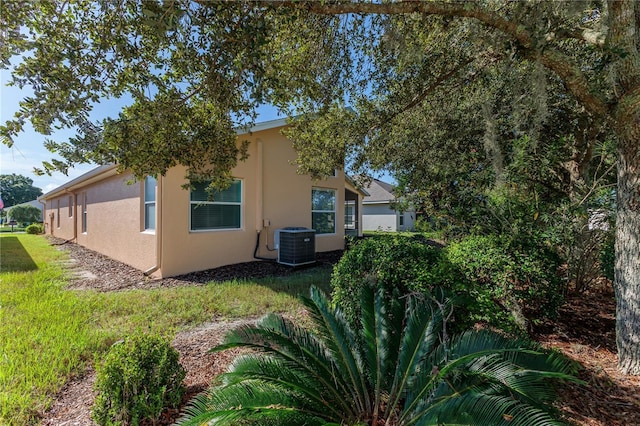 back of house featuring stucco siding, central AC unit, and a yard