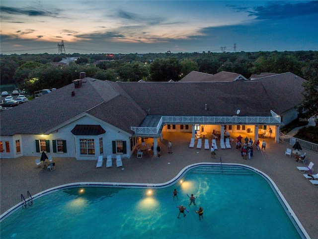 pool at dusk with fence, an outdoor pool, and a patio area