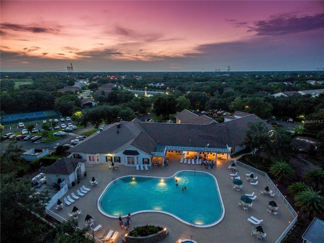 pool at dusk with a community pool and a patio