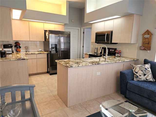 kitchen with light stone counters, fridge with ice dispenser, a peninsula, and stainless steel microwave