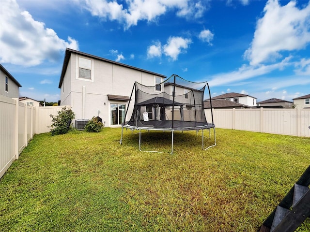 back of house featuring a yard, central AC unit, and a trampoline