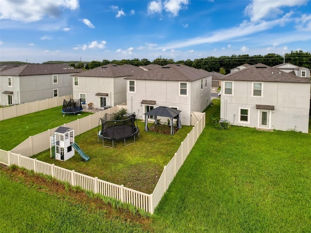 rear view of property featuring a trampoline, a playground, a yard, and a gazebo