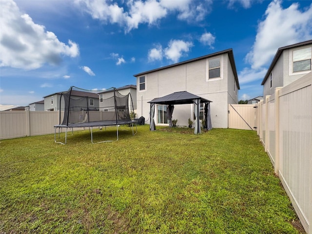 rear view of property featuring a trampoline, a yard, and a gazebo