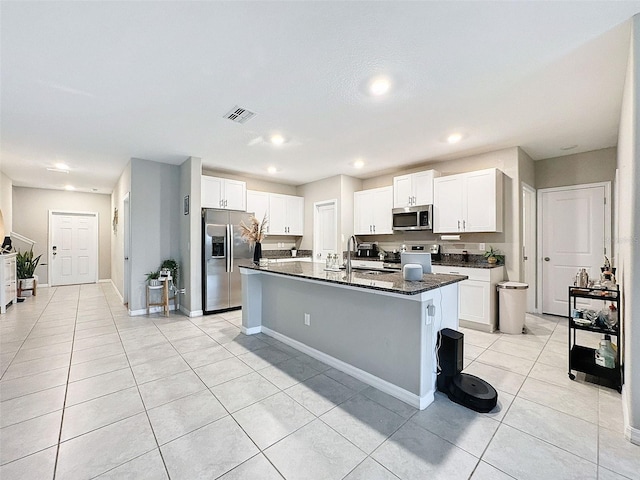 kitchen featuring dark stone counters, white cabinetry, stainless steel appliances, an island with sink, and sink