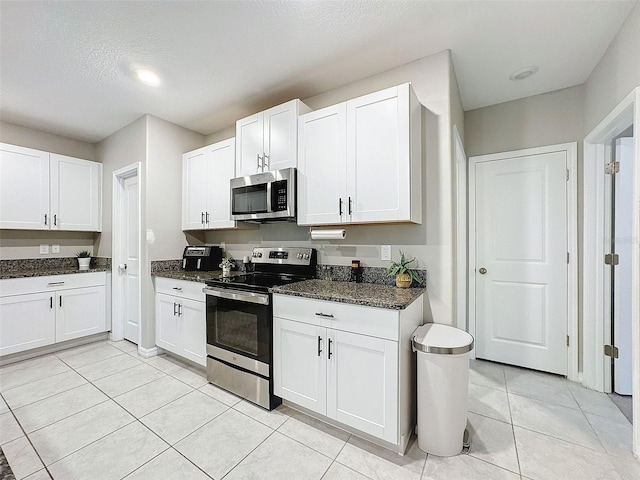 kitchen with stainless steel appliances, dark stone countertops, and white cabinetry