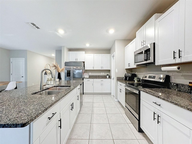 kitchen featuring a kitchen island with sink, white cabinetry, light tile patterned floors, stainless steel appliances, and sink