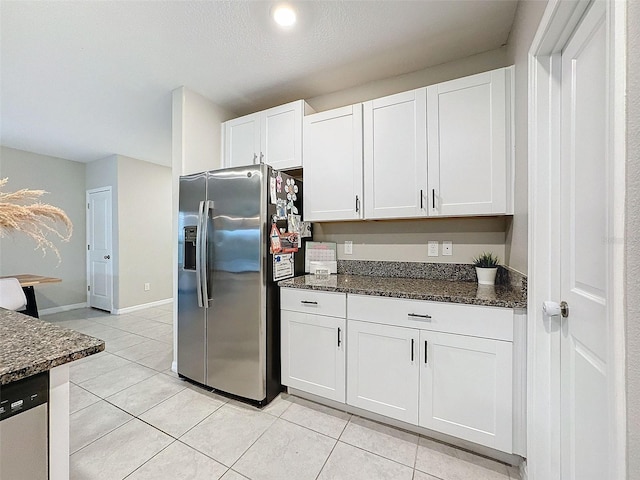 kitchen featuring dark stone counters, light tile patterned floors, appliances with stainless steel finishes, and white cabinets