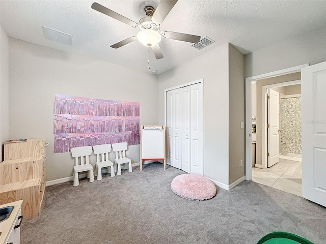 bedroom featuring a closet, light colored carpet, a textured ceiling, and ceiling fan