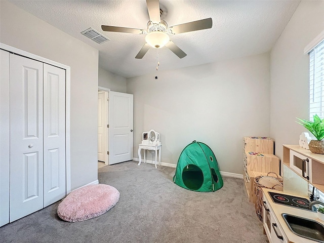 recreation room with a textured ceiling, ceiling fan, and light carpet