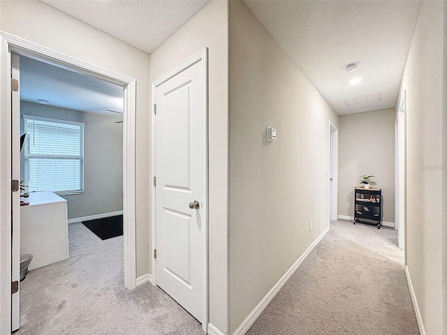 corridor featuring a textured ceiling and light colored carpet