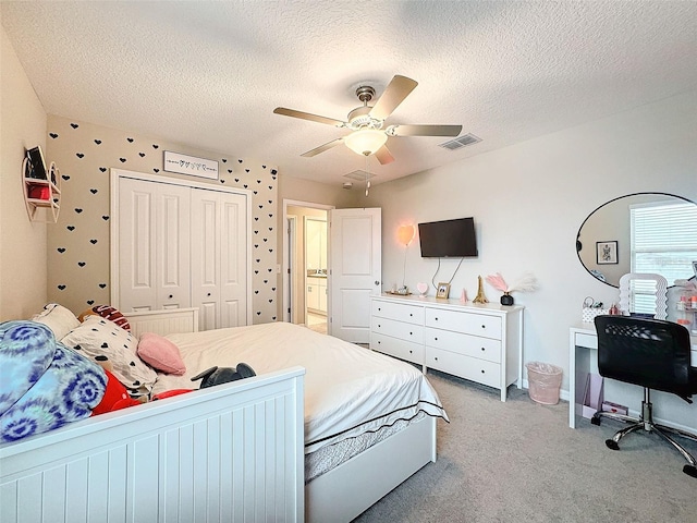 bedroom with a textured ceiling, ceiling fan, a closet, and light carpet