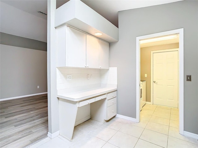 interior space featuring light tile patterned floors, light countertops, decorative backsplash, white cabinets, and washer / dryer