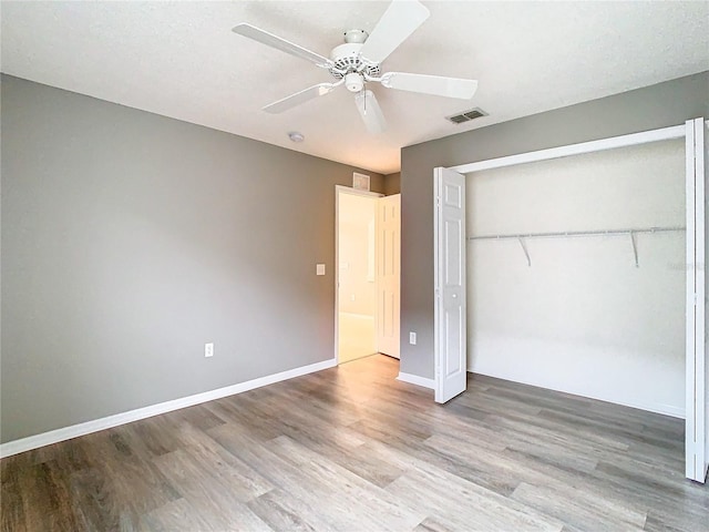 unfurnished bedroom with a closet, wood finished floors, visible vents, and baseboards