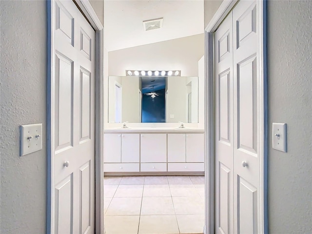 bathroom with double vanity, a textured wall, tile patterned floors, a sink, and a closet