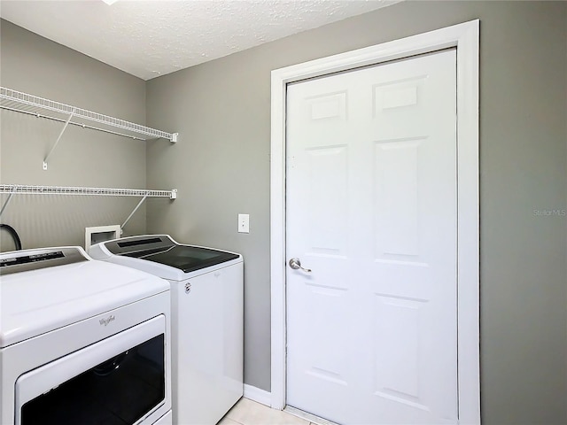 washroom with a textured ceiling, laundry area, light tile patterned floors, and washing machine and clothes dryer