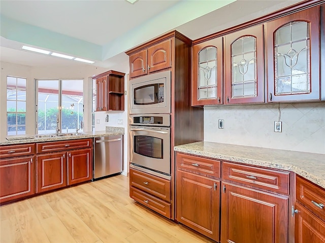 kitchen with light stone countertops, appliances with stainless steel finishes, backsplash, and light hardwood / wood-style floors