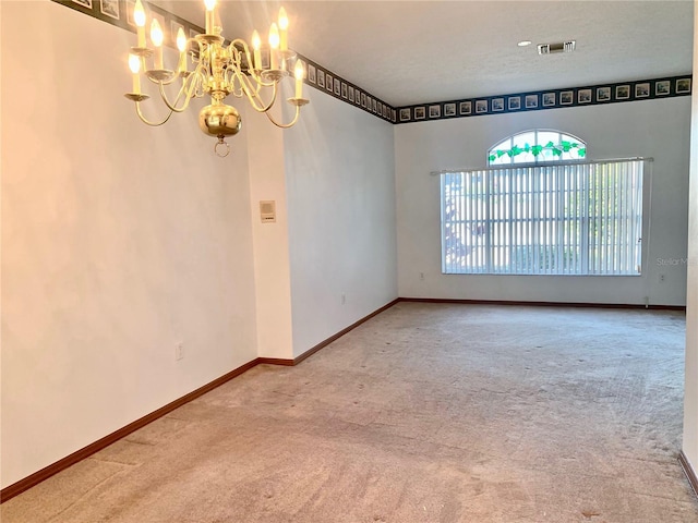 spare room with carpet floors, a notable chandelier, and a textured ceiling