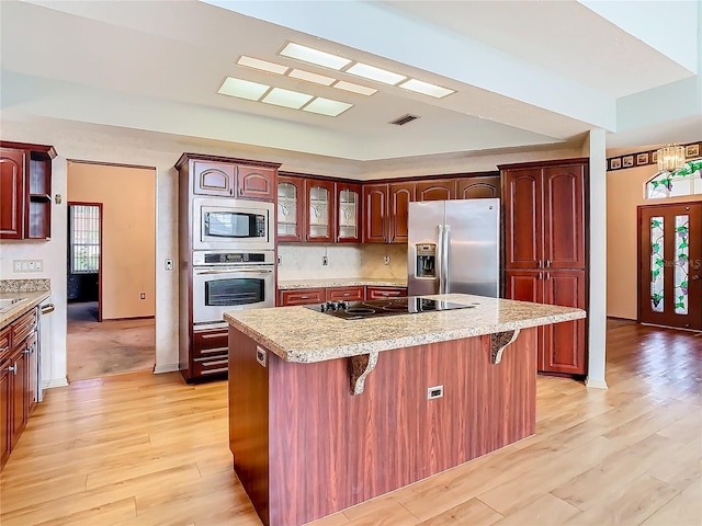 kitchen featuring appliances with stainless steel finishes, a center island, a kitchen bar, and light wood-type flooring