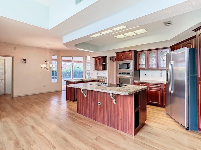 kitchen with appliances with stainless steel finishes, a breakfast bar area, a center island, a raised ceiling, and light hardwood / wood-style flooring