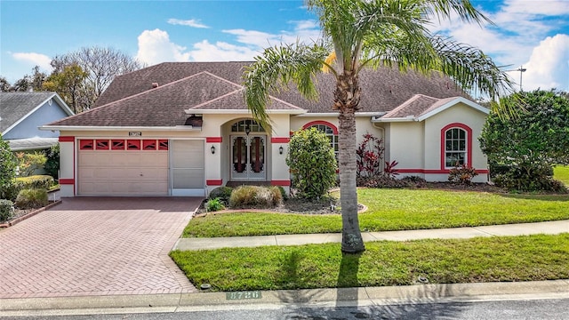 view of front of house featuring a garage, roof with shingles, decorative driveway, stucco siding, and a front lawn