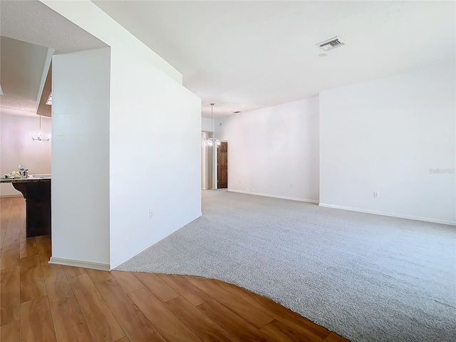 carpeted empty room featuring a chandelier, visible vents, baseboards, and wood finished floors