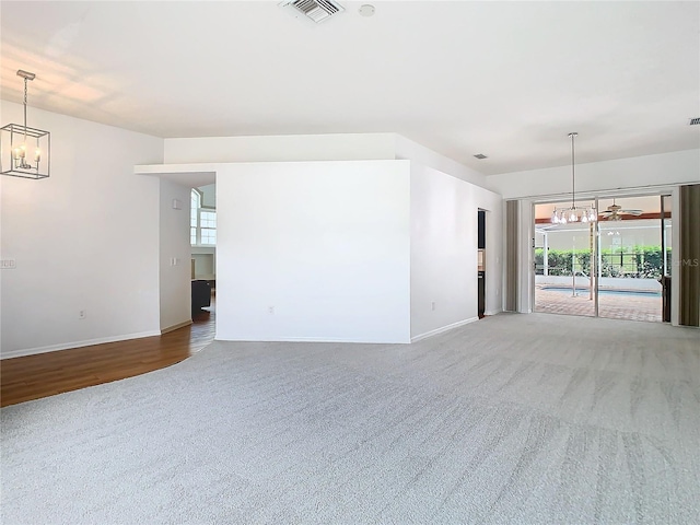 carpeted spare room featuring a chandelier, visible vents, and baseboards