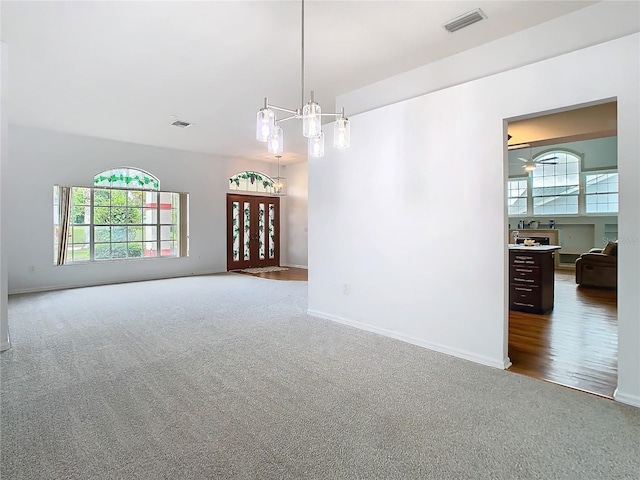 carpeted spare room with a chandelier, visible vents, and baseboards