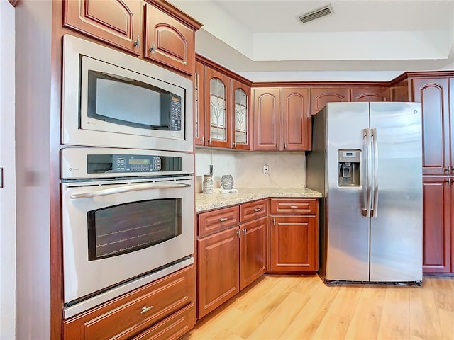 kitchen featuring light stone counters, light wood-style flooring, stainless steel appliances, visible vents, and glass insert cabinets