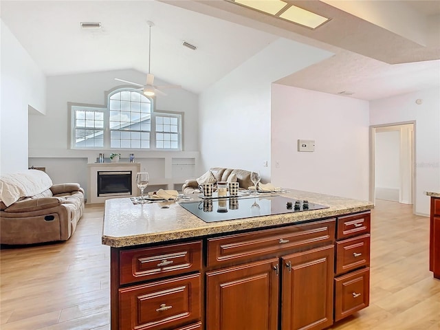 kitchen with lofted ceiling, light wood-style flooring, black electric cooktop, visible vents, and a glass covered fireplace