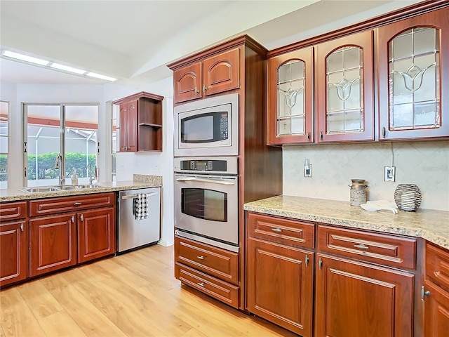 kitchen featuring stainless steel appliances, a sink, light wood-type flooring, light stone countertops, and glass insert cabinets