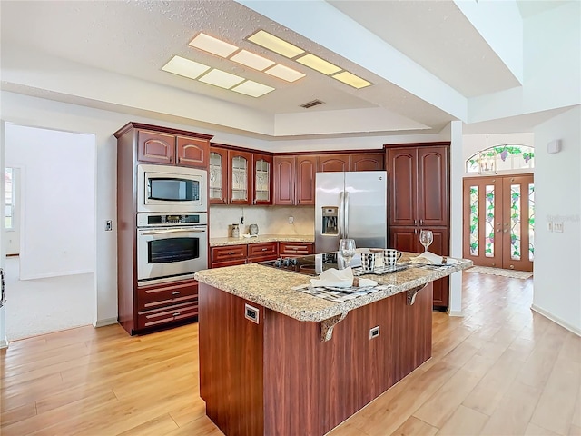 kitchen with a center island, a tray ceiling, stainless steel appliances, light wood-type flooring, and a kitchen bar