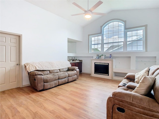 living room with vaulted ceiling, light wood-type flooring, a fireplace, and a ceiling fan