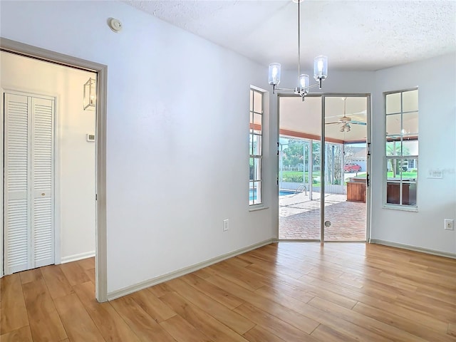 empty room featuring light wood finished floors, baseboards, a textured ceiling, and ceiling fan with notable chandelier