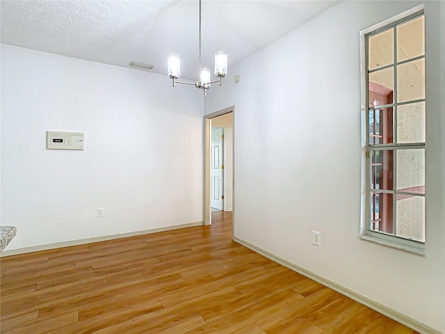 unfurnished room featuring a chandelier, light wood-type flooring, and baseboards