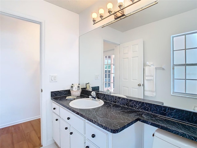 bathroom with toilet, baseboards, wood finished floors, and vanity