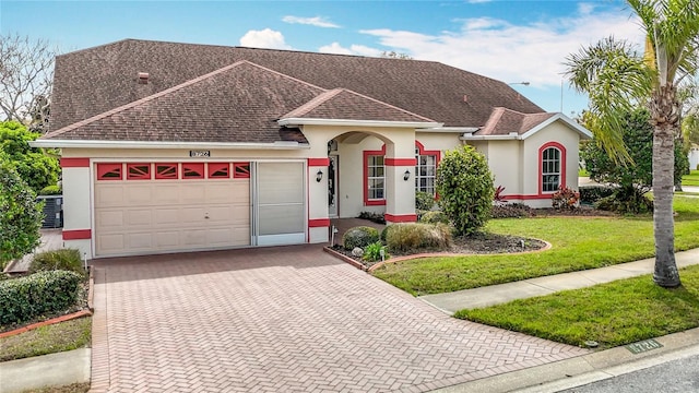 single story home featuring a shingled roof, an attached garage, decorative driveway, a front lawn, and stucco siding